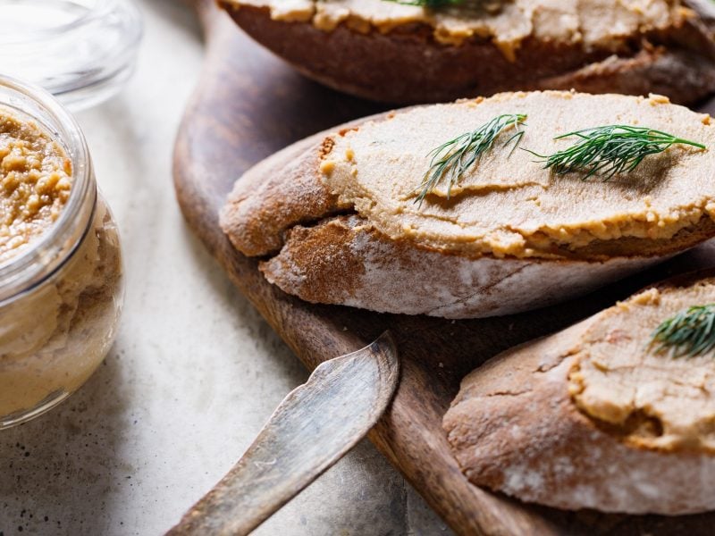 Draufblick, schräg: mehrere Scheiben Weißbrot, die mit einer Thunfischcreme mit Dill bestrichen sind. Daneben ist ein Glas mit der Creme sowie ein Messer.