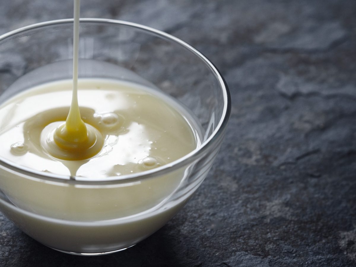 Vegane gezuckerte Kondensmilch wird von oben in eine Glasschale gegossen.