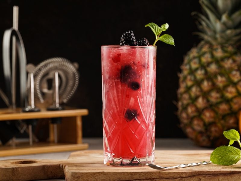 Alkoholfreier Bramble vor Baraccessoires, einer Ananas und einer Grapefruit.