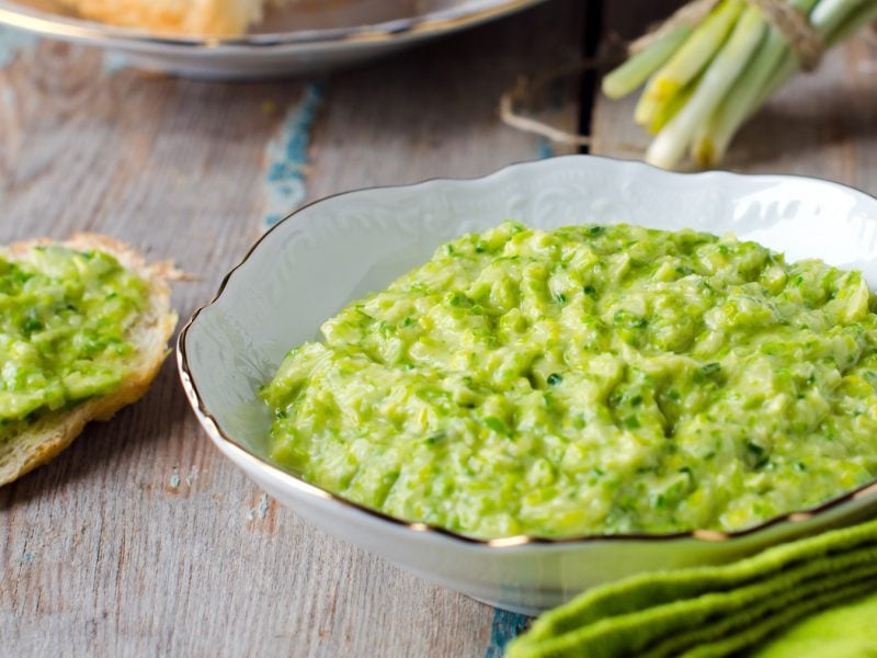 Eine weiße Schüssel mit der Bärlauch-Guacamole auf einem rustikalen Holztisch. Alles von schräg oben fotografiert.