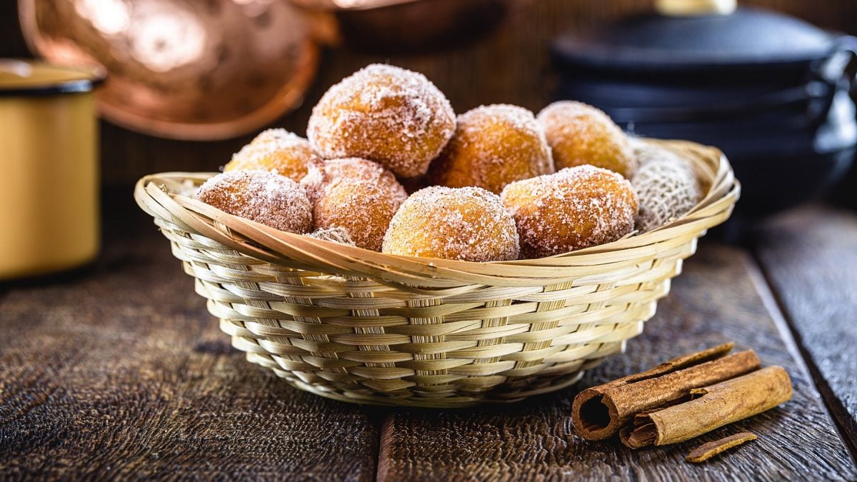 Bolinhos de chuva in einem Rattankorb. Daneben Zimtstangen