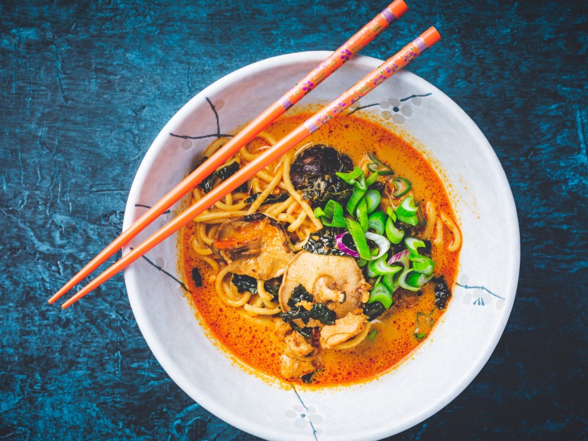 Eine weiße Schale mit der Curry-Suppe auf einem dunkelblauen Tisch. Alles direkt von oben fotografiert.