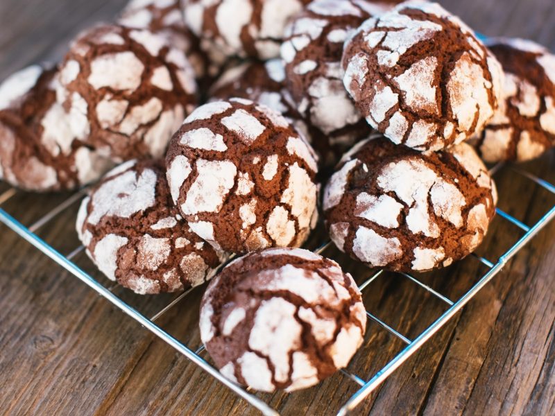 Draufsicht, schräg: Auf einem rustikalem Untergrund aus Holz liegt ein quadratisches Gitter auf dem Chocolate Crincle Cookies liegen.