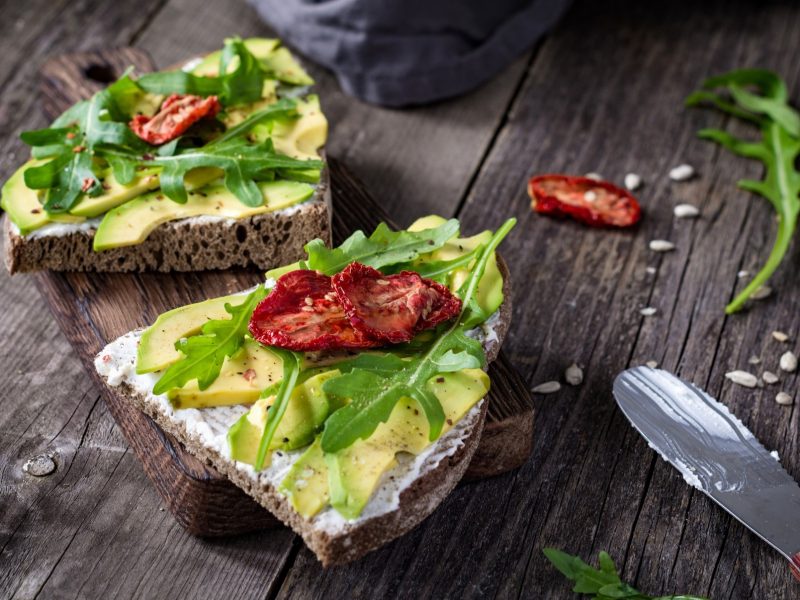 Draufsicht: Zwei Fancy-Avocado-Stullen liegen auf einem Holzbrettchen.