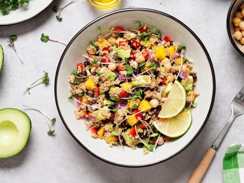 Draufblick: Auf einem hellen Untergrund steht eine runde Schüssel in der ein Quinoa-Salat mit Mango, Avocado, Bohnen ist.