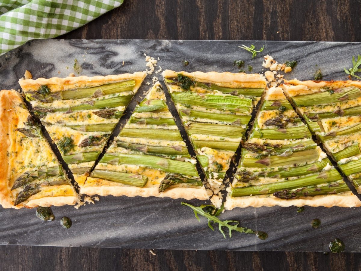 Draufsicht: eine Spargel-Quiche mit Bärlauch-Käse auf einem dunklen Untergrund.