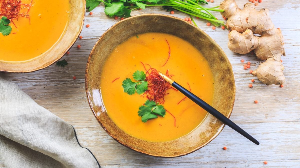 Miso-Suppe mit Ingwer und Karotten in einer Bowl. Rechts auf dem Bild Ingwer und Koriander, links unten ein Geschirrtuch. Der Hintergrund ist hellbraun.