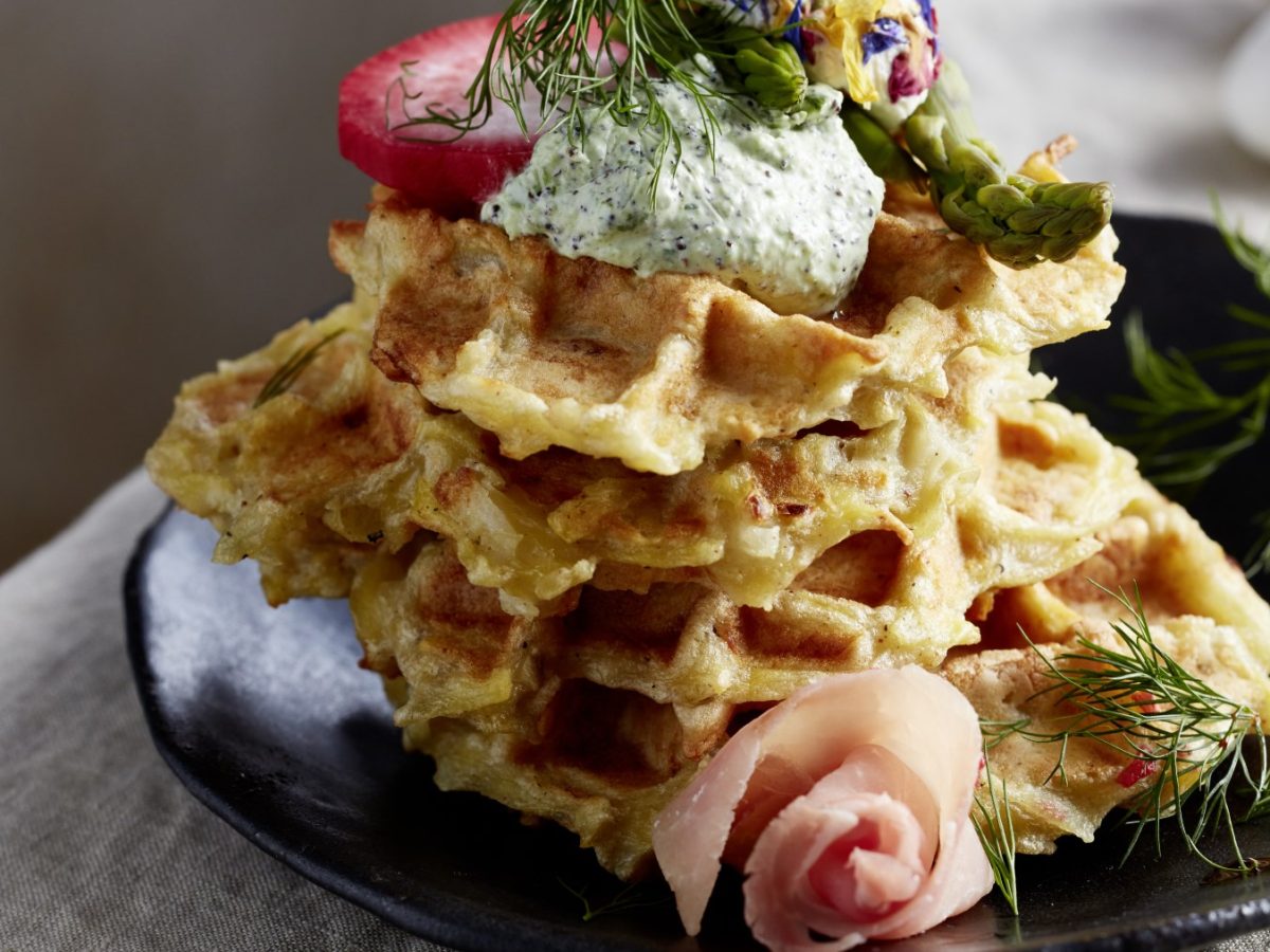 Knusprige Schmandwaffeln mit Antipasti auf einem schwarzen Teller auf einem beigen Hintergrund.