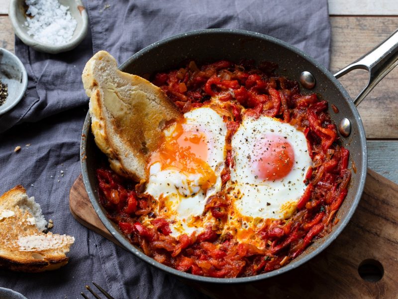 Paprikapfanne mit Nduja und zwei Eiern. Darin eine Scheibe Brot mit Butter. Von oben fotografiert.