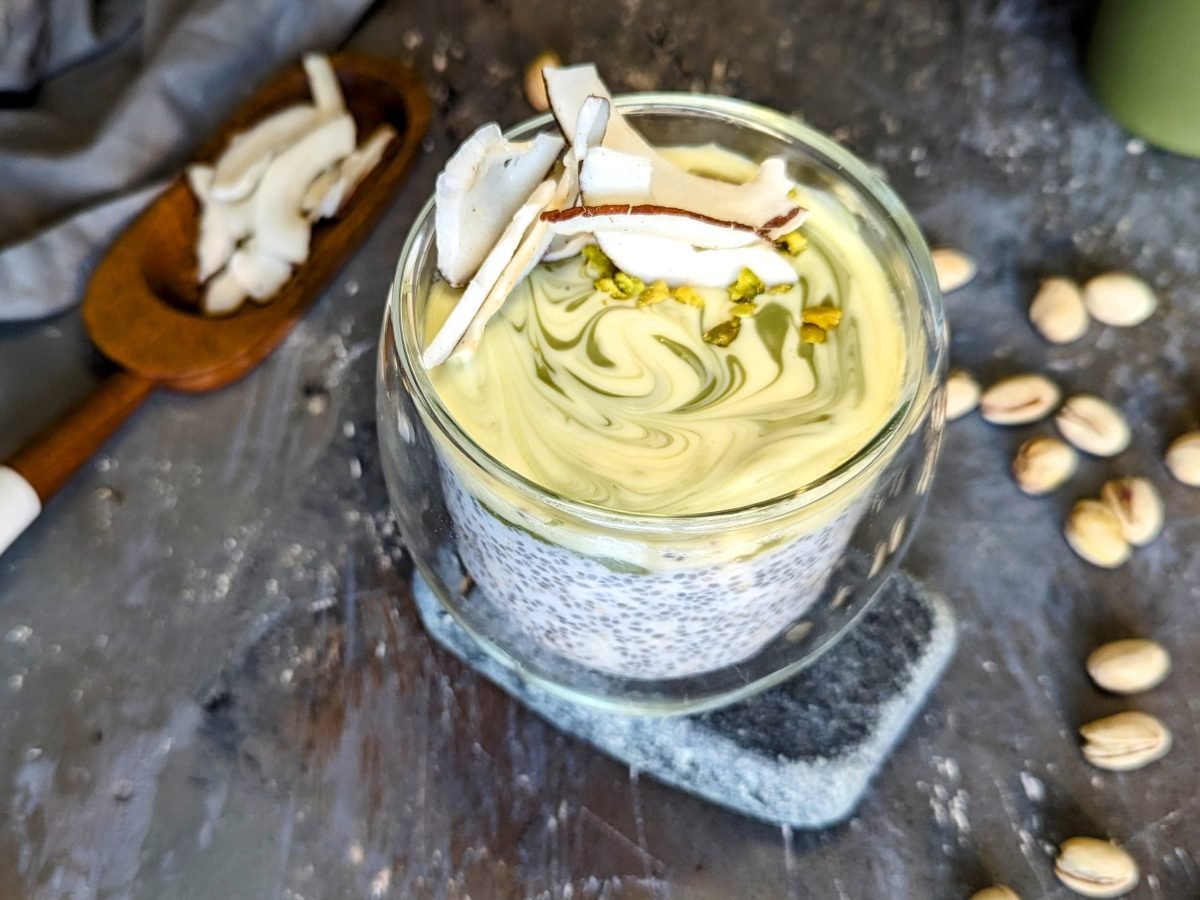 Das Glas mit der Kokos-Pistazien-Bowl auf einem Steintisch von schräg oben fotografiert.