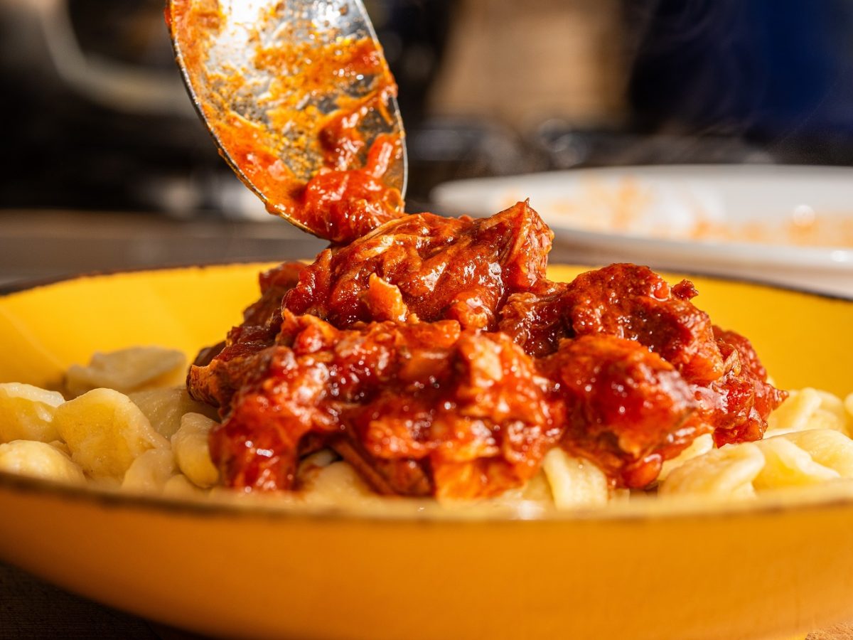 Ragù napoletano, dass mit einem Löffel auf Pasta auf einem gelben Teller gegeben wird.