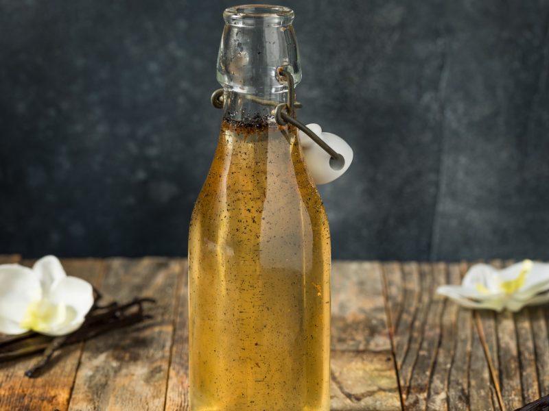 Eine Flasche mit dem Vanillesirup auf einem Holztisch mit grauem Hintergrund.