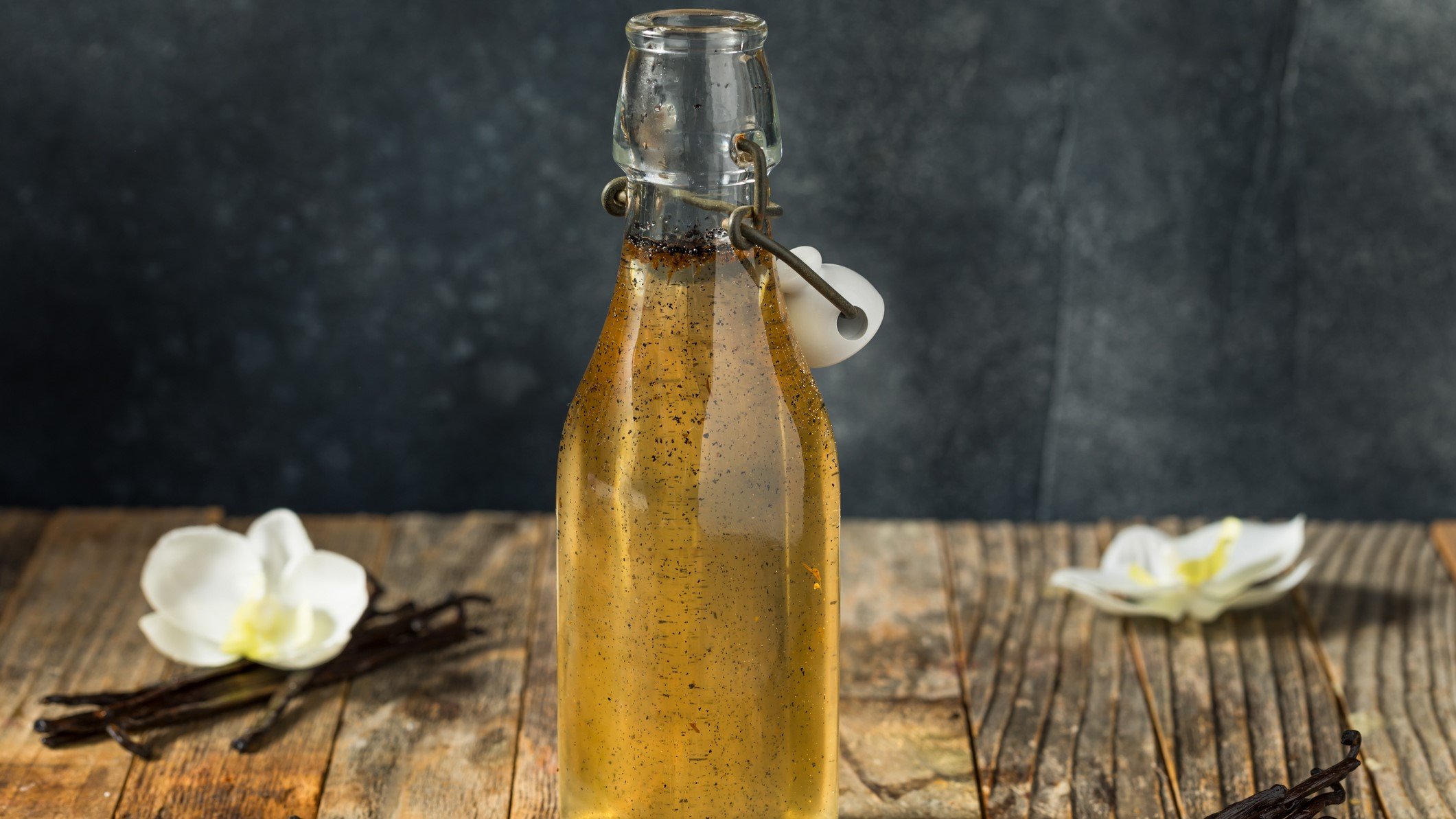 Eine Flasche mit dem Vanillesirup auf einem Holztisch mit grauem Hintergrund.