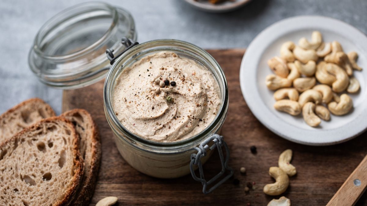 Vegane Foie Gras in einem Glas. Daneben Cashews und Brotscheiben.