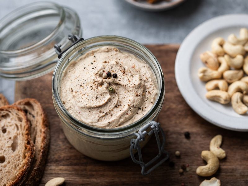 Vegane Foie Gras in einem Glas. Daneben Cashews und Brotscheiben.