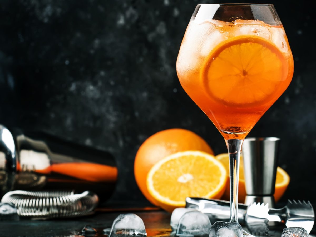 Aperol Spur in einem Glas. Im Hintergrund Orangen und Barzubehör.