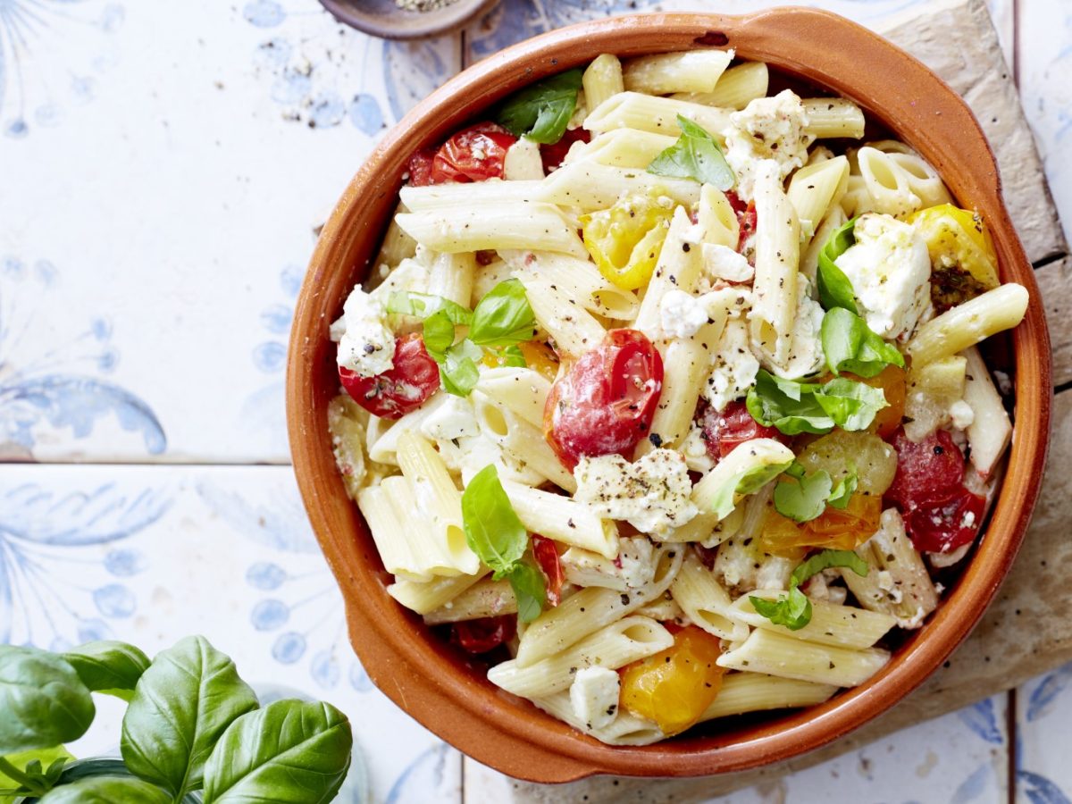 Baked Feta Pasta mit frischen Basilikum in runder Ofenform auf hellem Untergrund.