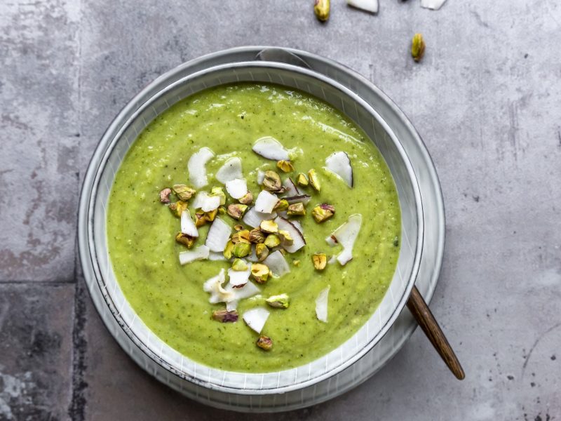 Eine helle Schüssel mit der grünen Suppe auf grauem Untergrund. Alles direkt von oben fotografiert.