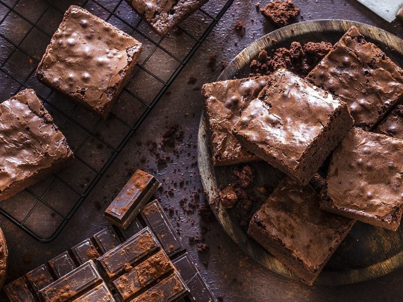 Frisch gebackene Brownies in Nahaufnahme mit sichtbaren Schokoladenstückchen und Kakao bestäubt.