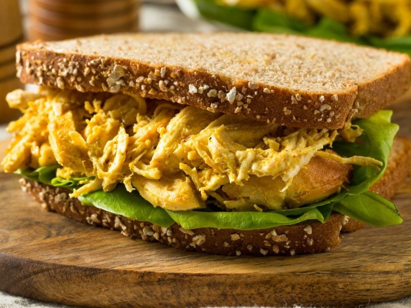 Frontal: Ein Coronation-Chicken-Sandwich auf einem Holzbrettchen.