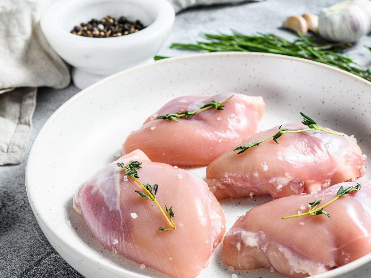 Draufsicht schräg: Auf einem Tisch liegt eine helle, runde Schale. In der liegen vier Hühnerfilets, die mit einem Thymianzweig und Salz belegt würden. / Hygiene-Regeln bei Geflügel