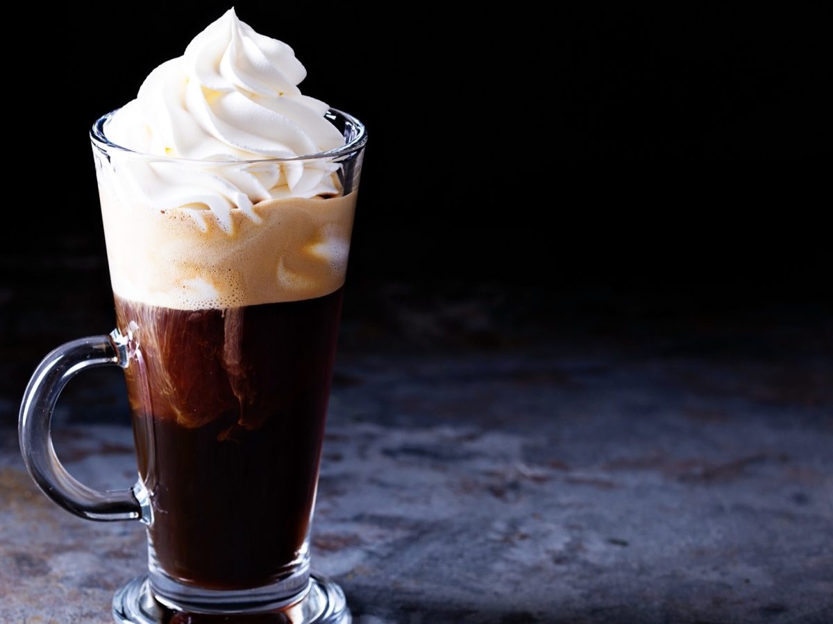 Frontal: Ein Glas Wiener Eiskaffee mit einer Sahnehaube steht auf einem Boden aus Holz.