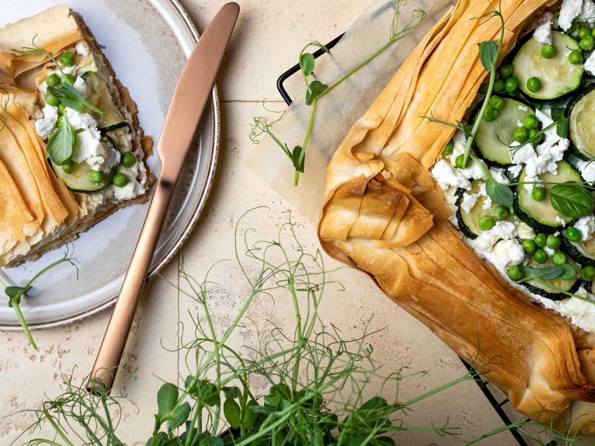 Frühlingstarte aus Filoteig mit Feta, Zucchini und Ebsen. Daneben ein Stück der Tarte auf einem Teller.