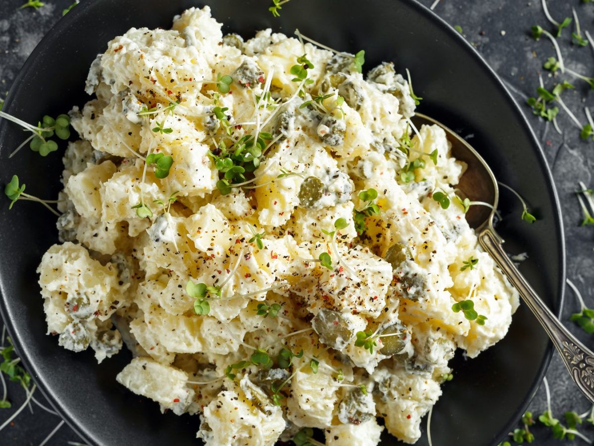 Schwarzer Teller mit cremigem Kartoffelsalat. Alles direkt von oben fotografiert.