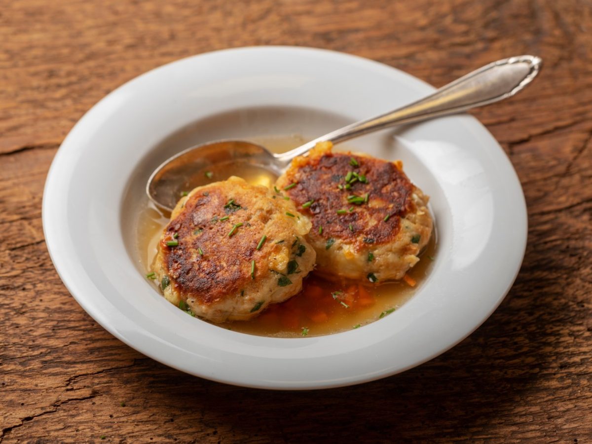 Kaspressknödel in einem weißen Suppenteller auf hölzernem Hintergrund.