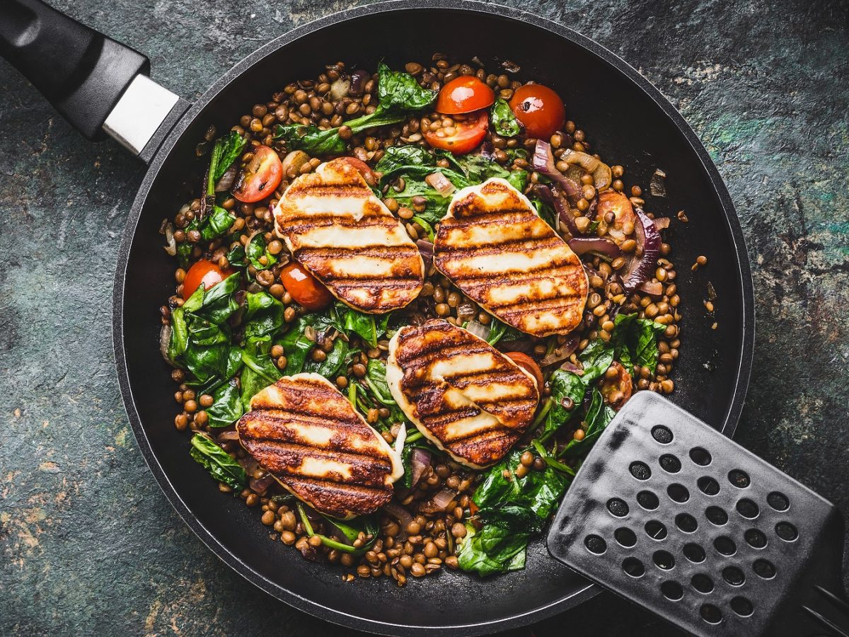 Linsen-Spinat-Gemüse mit Halloumi und Cherrytomaten in einer Pfanne von oben fotografiert.