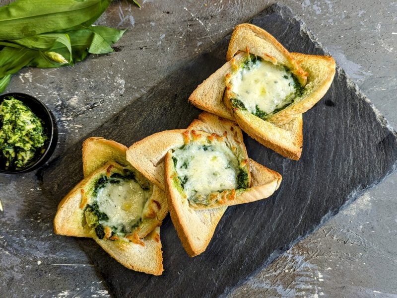 Drei Twisted Toasts mit Bärlauchbutter und Käse überbacken auf einer schwarzen Schieferplatte. Alles von oben fotografiert.