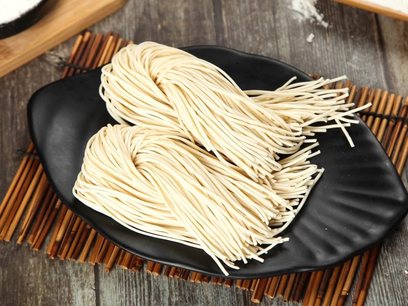 Selbstgemachte Ramen auf einem schwarzen Teller und Bambusmatte. Alles auf einem rustikalen Holztisch von schräg oben fotografiert.