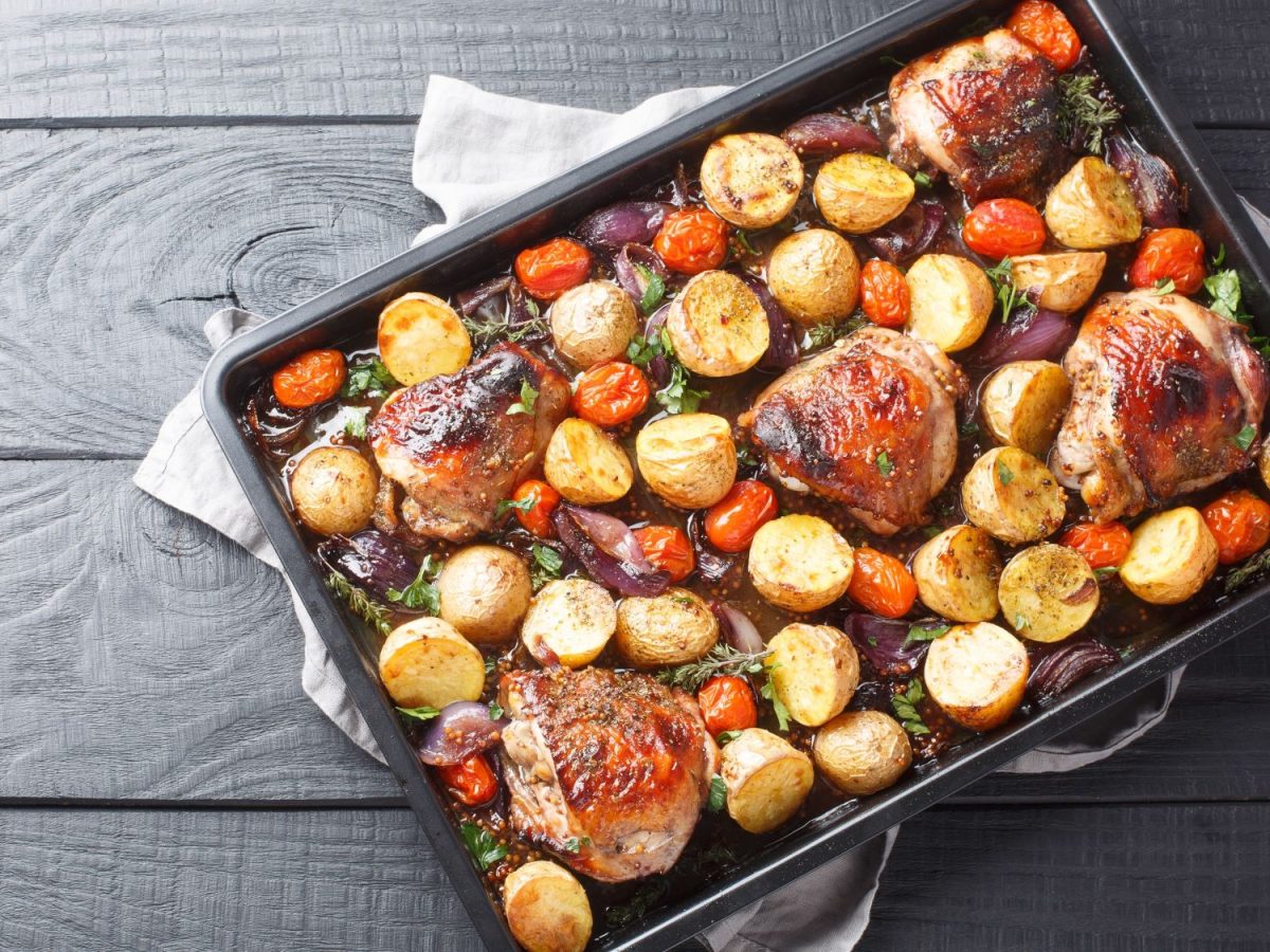 Draufsicht auf Balsamico-Hähnchen mit Kartoffeln und Tomaten vom Blech mit Kräutern.