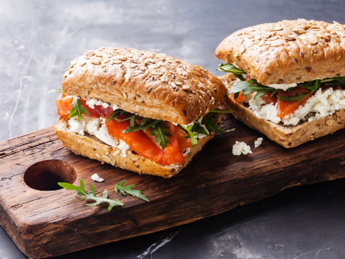 Zwei Brötchen mit Lachs und körnigem Frischkäse auf einem rustikalen Holzbrett von schräg oben fotografiert.