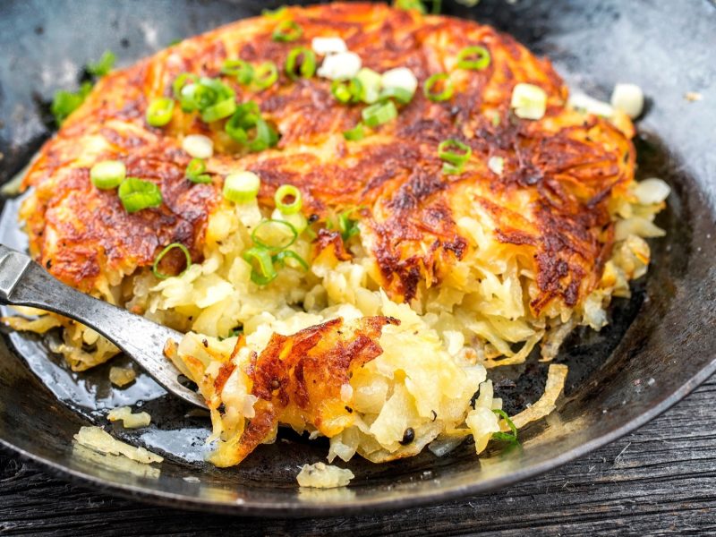 Draufsicht schräg: Eine schwarze gusseiseren Pfanne mit knusprig gebratenen Berner Rösti.