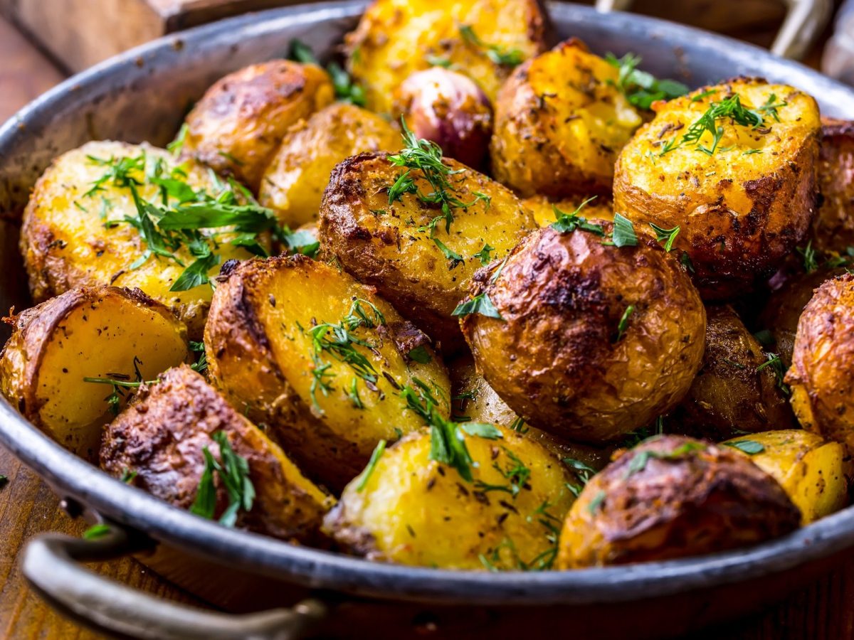 Draufsicht, schräg: gebratene Dill-Kartoffeln aus der Bratpfanne auf einem rustikalen Untergrund aus Holz.