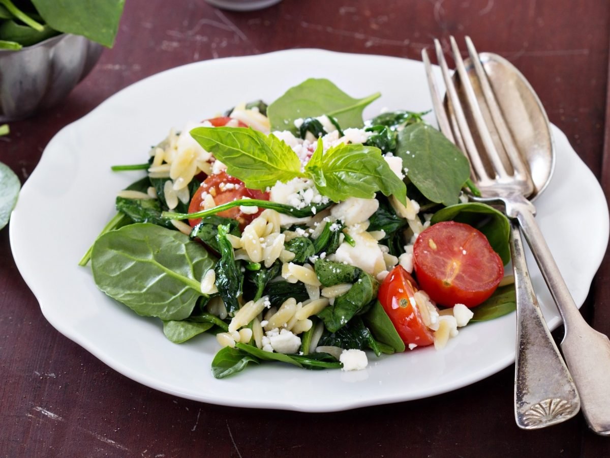 Draufsicht, schräg: Ein weißer Teller mi Orzo-Spinat-Salat.