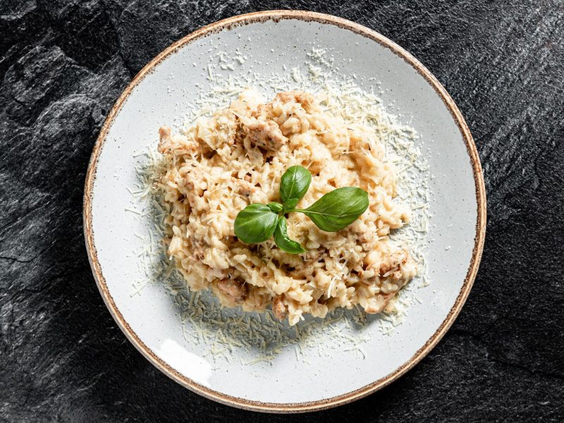 Draufsicht: Auf schwarzem Untergrund liegt ein weißer Teller mit einem Hähnchen-Risotto / Risotto-Rezept mit Hühnchen