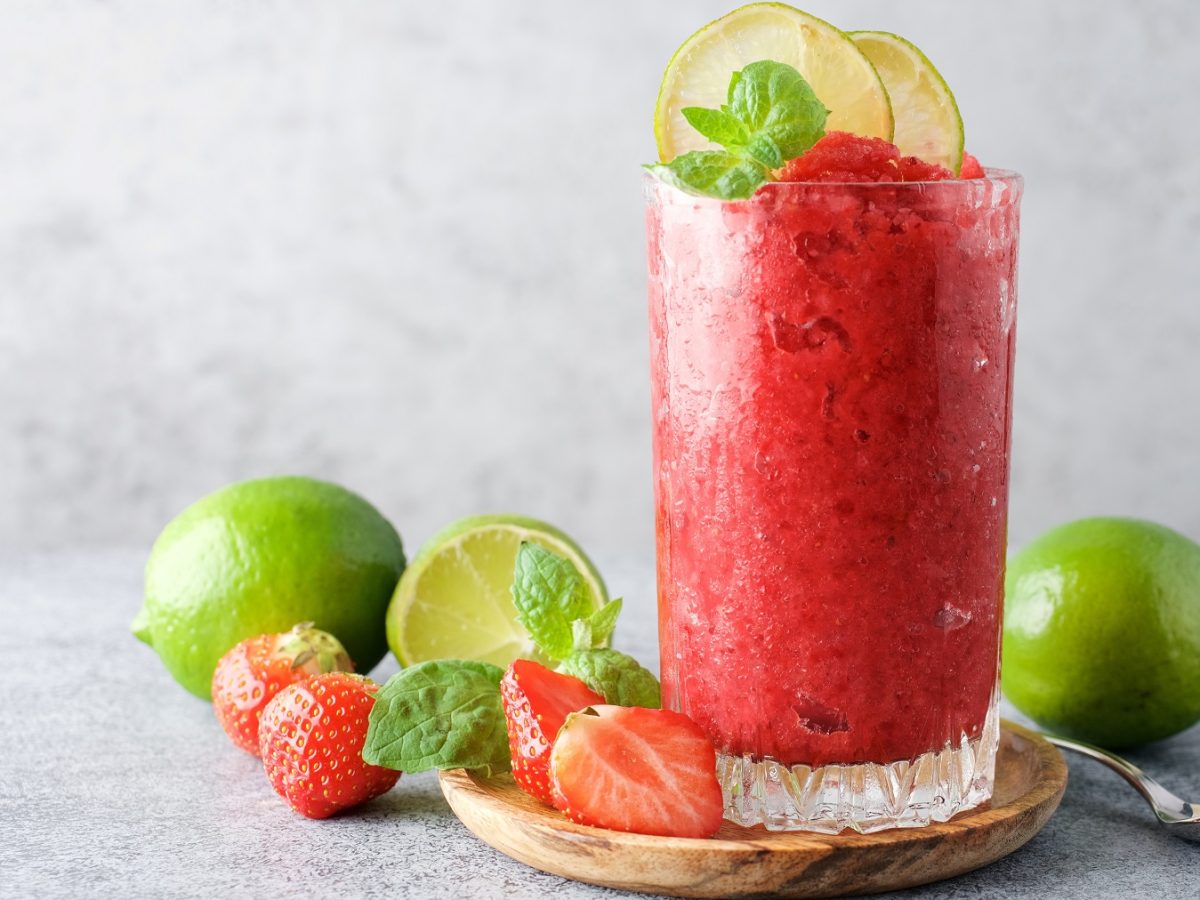 Erdbeerlimes-Granita in einem hohen Glas, dekoriert mit frischen Limetten und Minze.