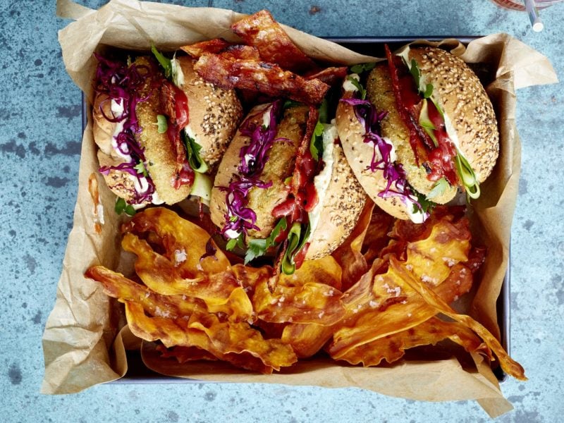 Draufsicht: Falafel Bacon Burger mit Süßkartoffelchips in viereckiger Form auf blauem Untergrund.