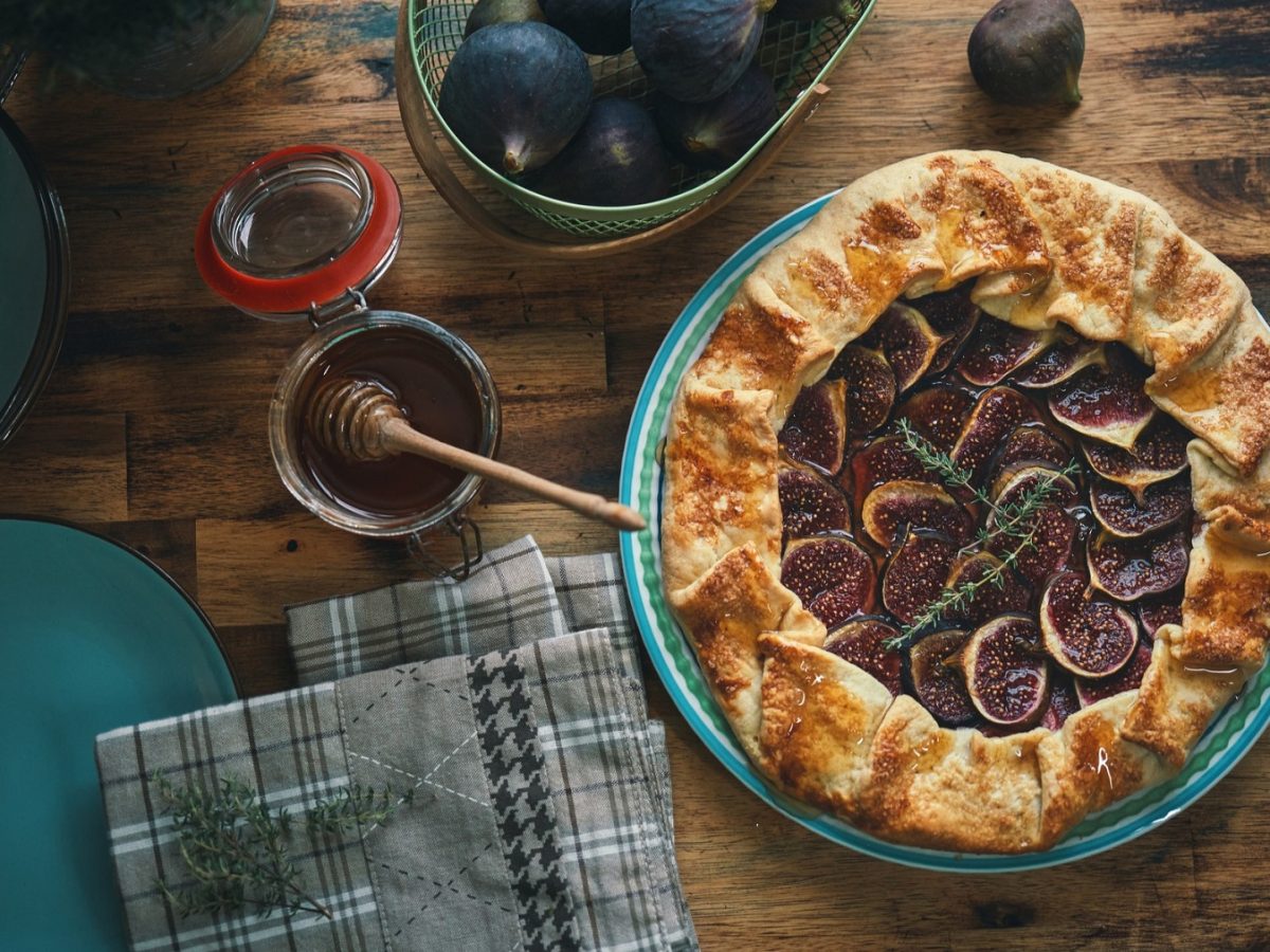 Hausgemachte Feigengalette auf Holztisch, garniert mit Thymian, neben Honig und türkisfarbenen Tellern.