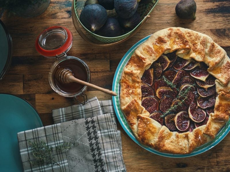 Hausgemachte Feigengalette auf Holztisch, garniert mit Thymian, neben Honig und türkisfarbenen Tellern.