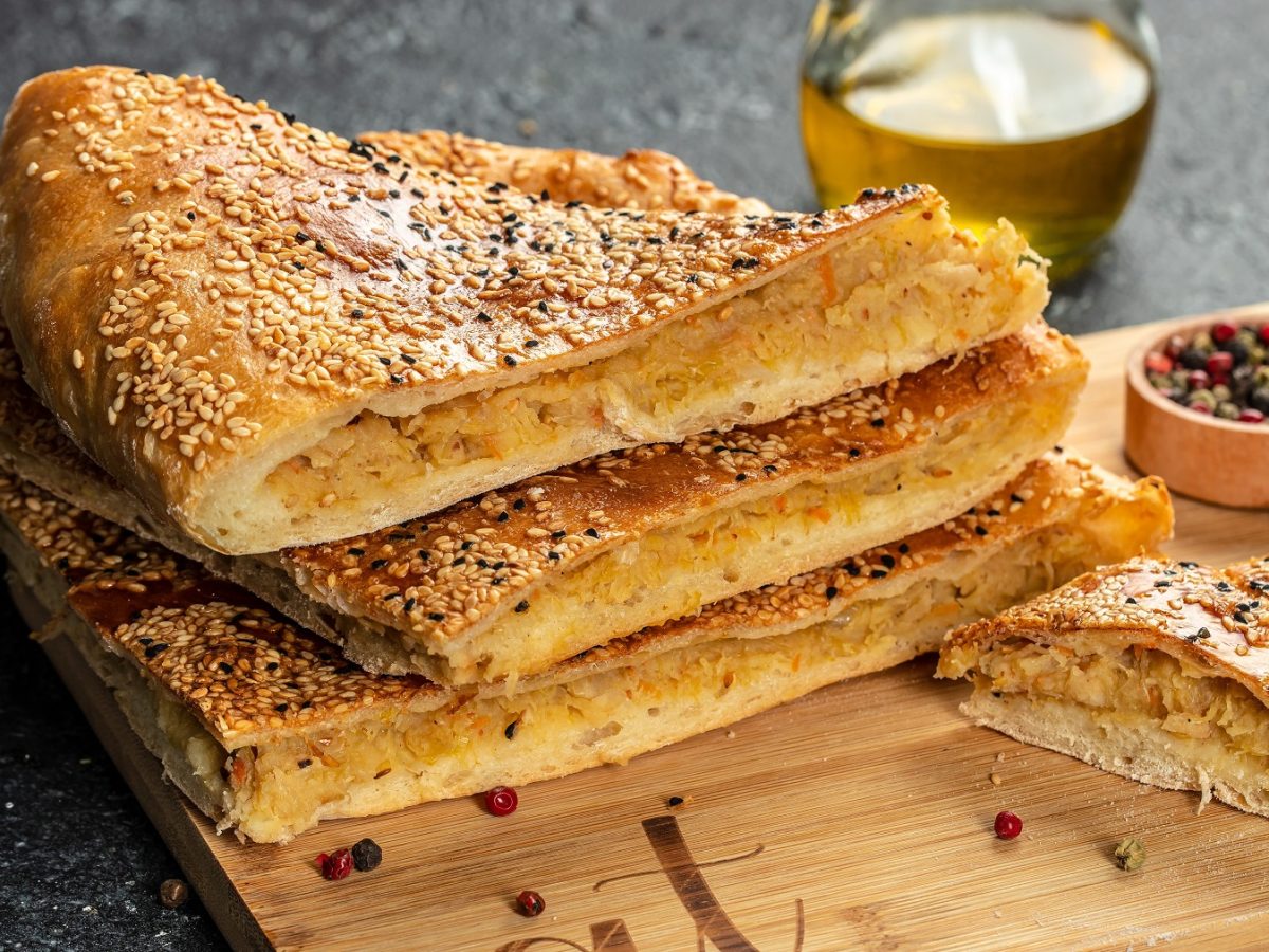 Gefüllte Fladenbrot übereinander gestapelt auf einem Holzbrett. Daneben eine Schale mit Gewürzen.