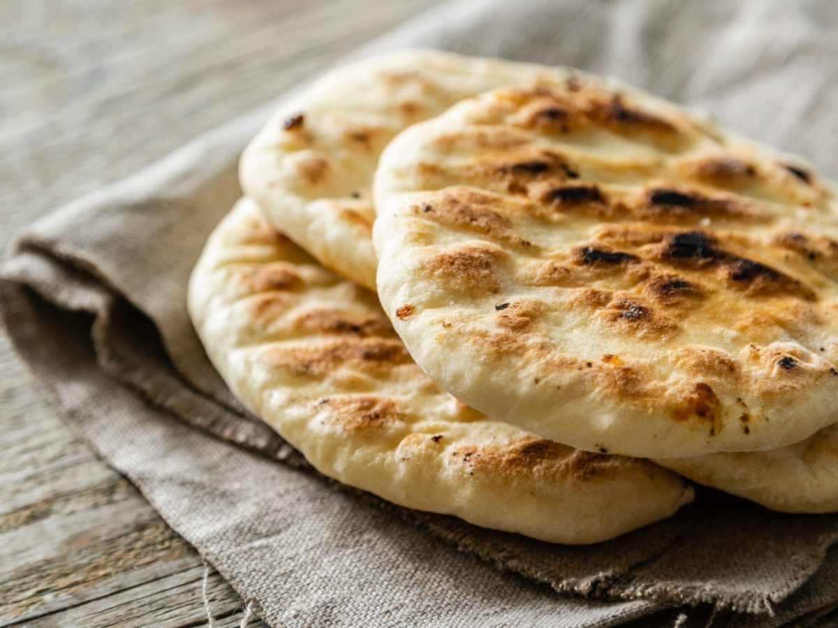 Glutenfreies Pita-Brot auf einem beigen Geschirrtuch auf braunem Hintergrund.