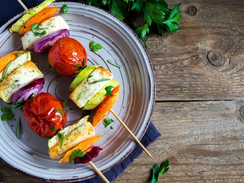 Halloumi-Grillspieße auf einem blauen Teller auf hölzernem Hintergrund.