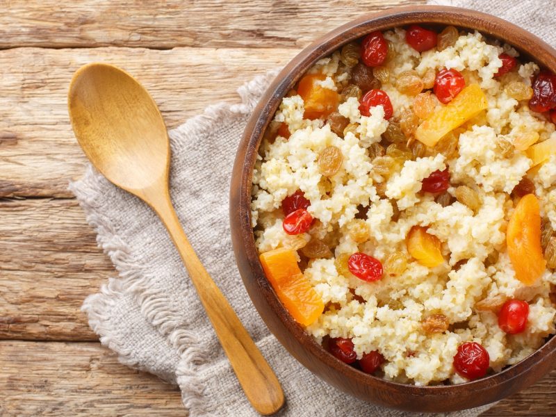 Hirse-Porridge mit getrockneten Aprikosen, Kirschen und Sultaninen in einer Holzschüssel.