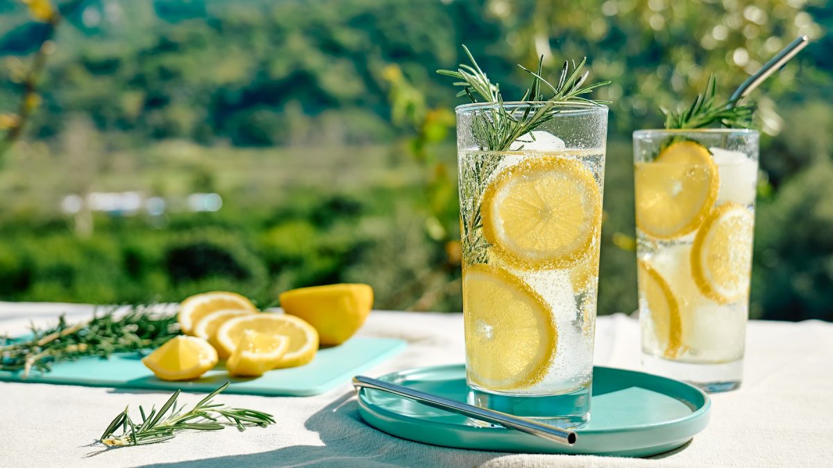 Ein weißer Tisch mit dem Italicus Spritz und grüner Natur im Hintergrund. Alles von der Seite fotografiert.