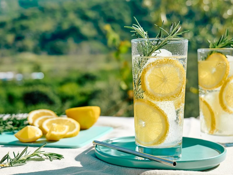 Ein weißer Tisch mit dem Italicus Spritz und grüner Natur im Hintergrund. Alles von der Seite fotografiert.