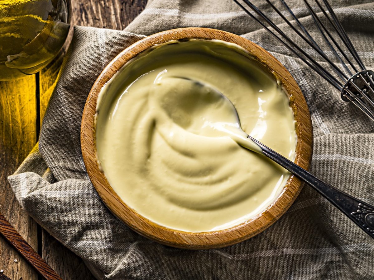 Keqpie Mayo in einem hölzernen Schälchen auf einem dunkelgrauen Geschirrtuch. Rechts ein Schneebesen und in der Schüssel ein Löffel.