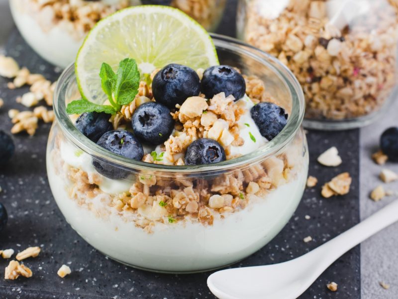 Joghurtparfait im Glass getoppt mit Granola, Blaubeeren, Limettenscheibe und Limettenzeste.